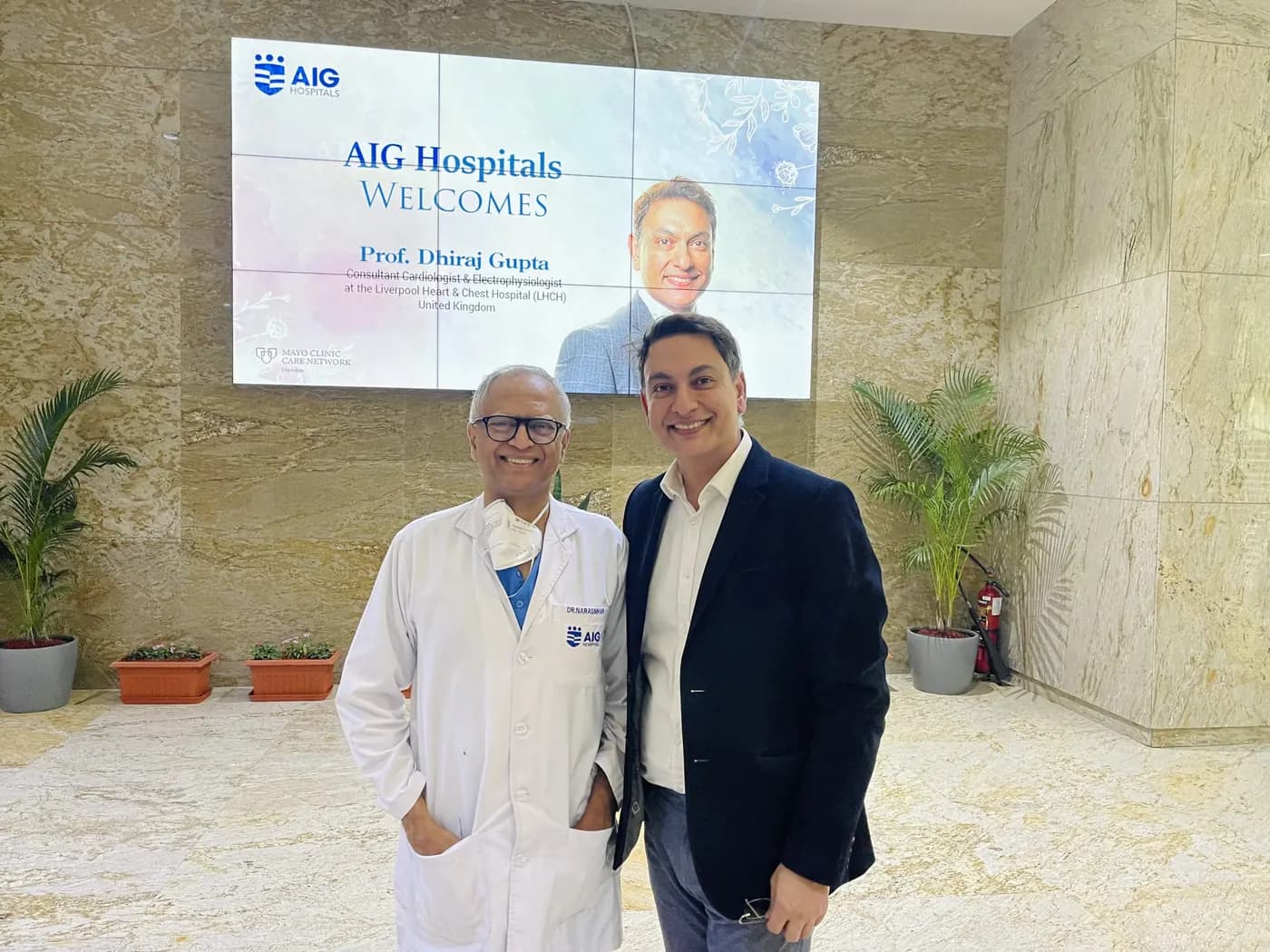 Professor Gupta with a fellow cardiologist at AIG Hospitals Hyderabad in 2022, beneath a screen welcoming him to the hospital.